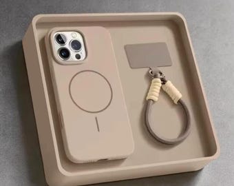 Pode incluir: Uma capa de telefone bege com um design circular e uma pulseira de pulso a condizer, apresentada numa bandeja quadrada. A capa é projetada para um smartphone, e a pulseira de pulso tem um laço para facilitar o transporte. A bandeja também é bege.