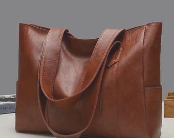 Pode incluir: Uma mala tote de couro castanho com duas alças e uma alça de ombro. A mala tem formato retangular com um bolso lateral. O couro tem um acabamento liso e polido. A mala está sobre uma superfície branca.