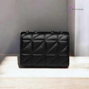 Puede incluir: Bolso negro acolchado con detalles plateados. El bolso presenta un patr&oacute;n geom&eacute;trico de diamantes y una forma rectangular. Tachuelas plateadas adornan la parte superior. El logotipo de The TotyBags est&aacute; en la esquina superior derecha.