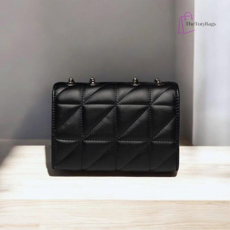 Puede incluir: Bolso negro acolchado con detalles plateados. El bolso presenta un patr&oacute;n geom&eacute;trico de diamantes y una forma rectangular. Tachuelas plateadas adornan la parte superior. El logotipo de The TotyBags est&aacute; en la esquina superior derecha.