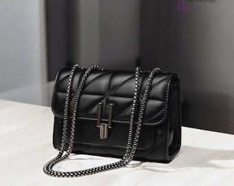 Pode incluir: Bolsa transversal preta acolchoada com corrente prateada. A bolsa tem formato retangular com fecho de aba e fecho de metal prateado. O logotipo TotyBags está no canto superior direito.