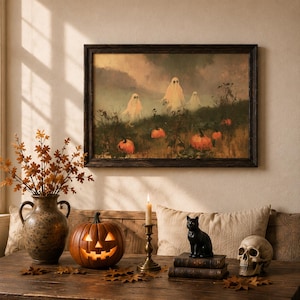 Puede incluir: Una impresión artística enmarcada que representa tres fantasmas en un campo de calabazas, exhibida con un jarrón de cerámica con hojas de otoño, una calabaza iluminada, un candelabro de latón, una figura de gato negro sobre libros y un cráneo.