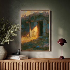 Könnte beinhalten: Ein gerahmter Wandkunstdruck, der ein Steingebäude mit einer offenen Tür und einem daneben stehenden Holzkreuz zeigt. Die Szene wird von hellem goldenen Licht beleuchtet, das lange Schatten auf den Boden wirft, mit blauen und grünen Tönen.