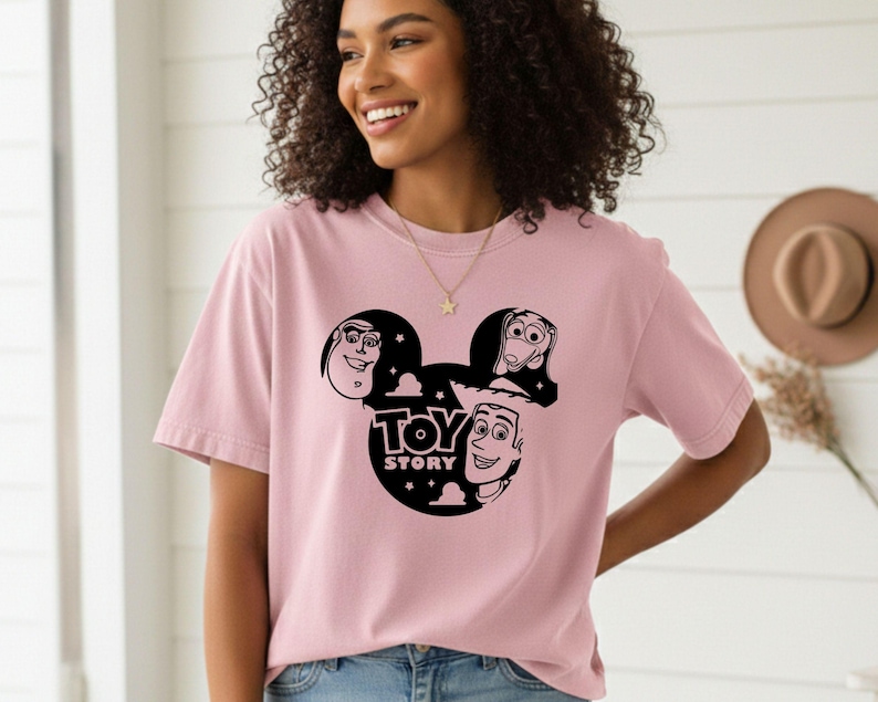 K&ouml;nnte beinhalten: Hellrosa T-Shirt mit schwarzer Grafik von Toy Story-Charakteren in einer Mickey Mouse-Silhouette. Der Text "TOY STORY" ist ebenfalls schwarz. Das T-Shirt hat einen l&auml;ssigen Stil.
