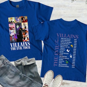 Op de afbeelding: Twee koningsblauwe t-shirts met de tekst "VILLAINS THE EVIL TOUR". E&eacute;n shirt heeft een collage van schurkenpersonages. Het andere shirt geeft schurken en hun debuutjaren weer. Een spijkerbroek en witte sneakers staan ook op de afbeelding.