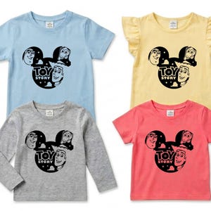K&ouml;nnte beinhalten: Vier Kinder-T-Shirts in Hellblau, Gelb, Grau und Koralle. Jedes Shirt zeigt eine schwarze Grafik von Toy Story-Charakteren in einem Mickey-Mouse-f&ouml;rmigen Design mit den Worten "TOY STORY" darunter. Das gelbe Shirt hat R&uuml;schen&auml;rmel.