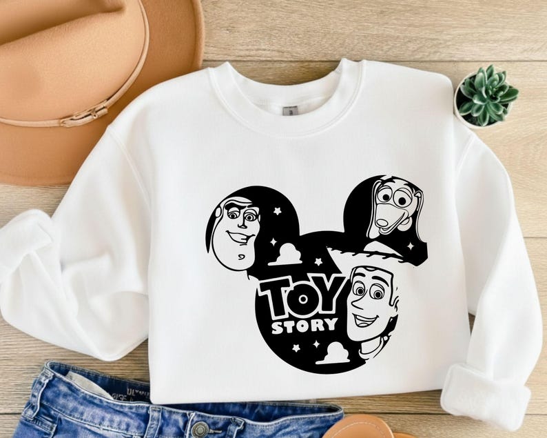 K&ouml;nnte beinhalten: Wei&szlig;es Sweatshirt mit Rundhalsausschnitt und schwarzer Grafik der Toy Story-Charaktere Buzz Lightyear, Slinky Dog und Woody in einem von Mickey Mouse inspirierten Design. Die Worte "Toy Story" sind ebenfalls in der Grafik enthalten.