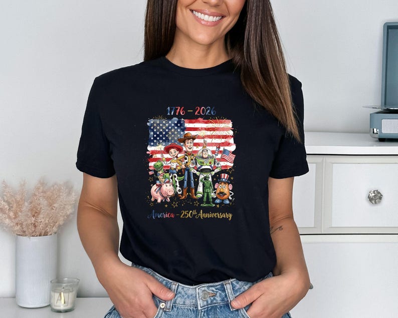 May include: Black t-shirt featuring a graphic of the American flag with the text "1776-2026" and a group of cartoon characters. The text "America - 250th Anniversary" is below the characters.
