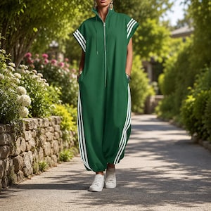 Puede incluir: Mono verde con rayas blancas en los laterales y las mangas. Tiene una cremallera frontal y bolsillos. La persona lleva zapatillas blancas. El fondo muestra un camino bordeado de &aacute;rboles.