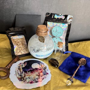 May include: A collection of ritual items including a round glass bottle with a cork stopper and twine, a small clear vial, a blue velvet pouch, a metal spoon with a crystal handle, a sticker with a desert landscape, and two black pouches.