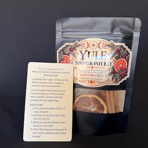 May include: A black pouch labeled Yule Simmer Pot with a clear window showing dried orange slices and cinnamon sticks, accompanied by a cream-colored instruction card detailing how to use the seasonal botanical blend for simmering.