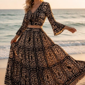 May include: A two-piece set consisting of a long-sleeved crop top with a V-neckline and a matching floor-length maxi skirt. Both pieces feature a bold, repeating black and beige botanical print with intricate symmetrical patterns throughout.