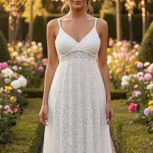 Puede incluir: Un vestido blanco de encaje con escote en V y tirantes finos. El vestido presenta un corpiño detallado y una falda fluida. El fondo muestra un jardín con flores coloridas y vegetación, creando una estética romántica.