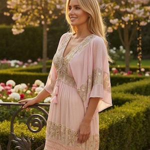 Pu&ograve; includere: Un abito lungo rosa chiaro con un profondo scollo a V con ricami dorati, ampie maniche a kimono e una coulisse con nappe in vita. La gonna presenta sezioni a balze con intricati motivi floreali dorati e dettagli in pizzo.