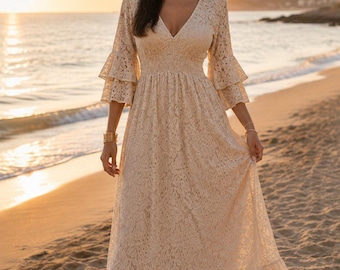 May include: A floor-length cream-colored lace dress featuring a V-neckline, a smocked waist, and three-quarter length sleeves with double-tiered ruffled cuffs. The skirt includes a wide ruffled hemline, creating a flowing silhouette.