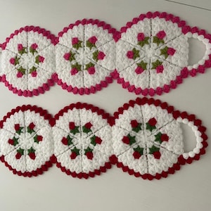May include: Two sets of handmade, white crochet coasters with a floral design. Each coaster has a scalloped edge and a handle. One set has pink accents, the other has red accents. The floral design includes green and pink or red accents.