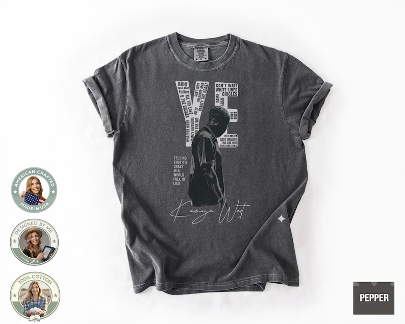 May include: Dark gray t-shirt featuring a graphic of a person and the text "YE" and "Kanye West". The shirt includes additional text elements. The shirt is made of 100% cotton.