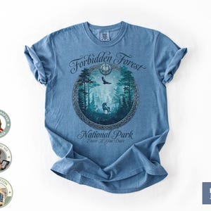 May include: Blue jean t-shirt with a circular graphic featuring a forest scene with a deer, eagle, and trees. The text reads "Forbidden Forest National Park Enter If You Dare". The shirt is made of 100% cotton.