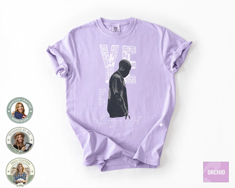 May include: A light purple t-shirt featuring a black and white image of a person and the text "YE" in white. Additional white text is arranged vertically on the right side of the image. The shirt has short sleeves and a crew neck.