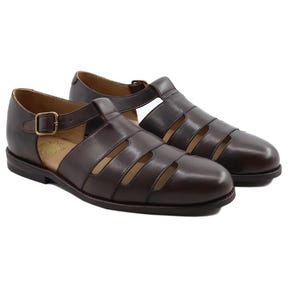 May include: A pair of dark brown leather sandals with an open design. The sandals feature multiple straps across the top and a buckle closure. The soles are a darker shade of brown.