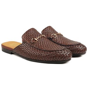 Könnte beinhalten: Ein Paar braune, gewebte Leder-Slipper mit goldfarbenen Metallakzenten. Die Schuhe haben einen niedrigen Absatz und ein klassisches Design, das sich für Freizeit- oder halbformelle Anlässe eignet.