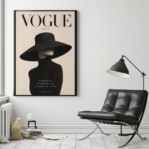 Può includere: Poster Vogue Paris incorniciato con una donna con cappello nero e dolcevita. Il logo Vogue è in alto, con testo francese sotto l'immagine. Il poster è in una cornice nera e appeso a una parete bianca.
