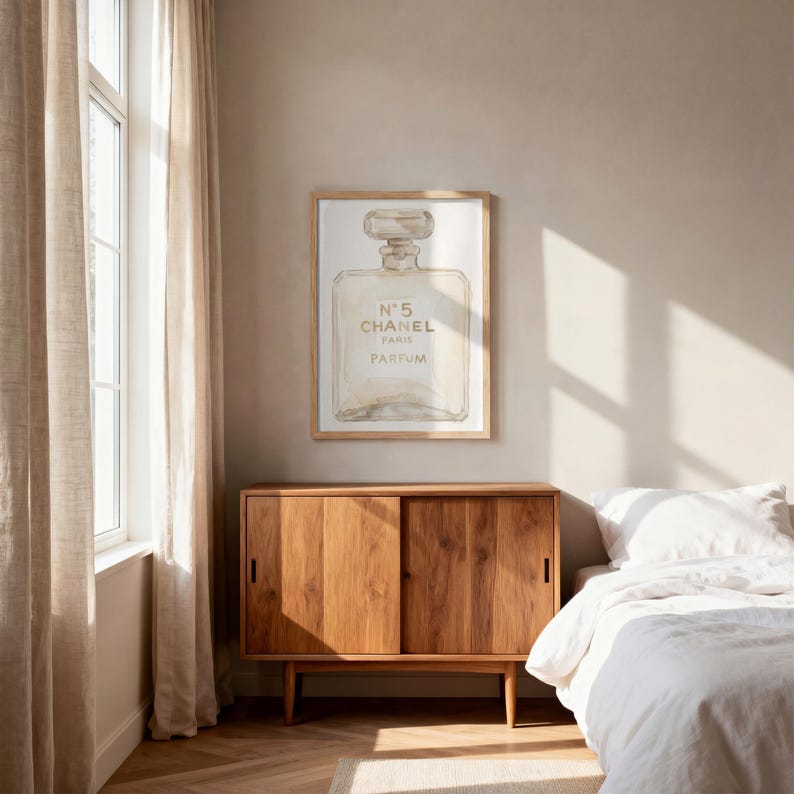 May include: A framed print featuring a watercolor illustration of a perfume bottle. The artwork displays the text "N&deg;5 CHANEL PARIS PARFUM" in a neutral color palette. The print is displayed above a wooden cabinet in a bedroom setting.