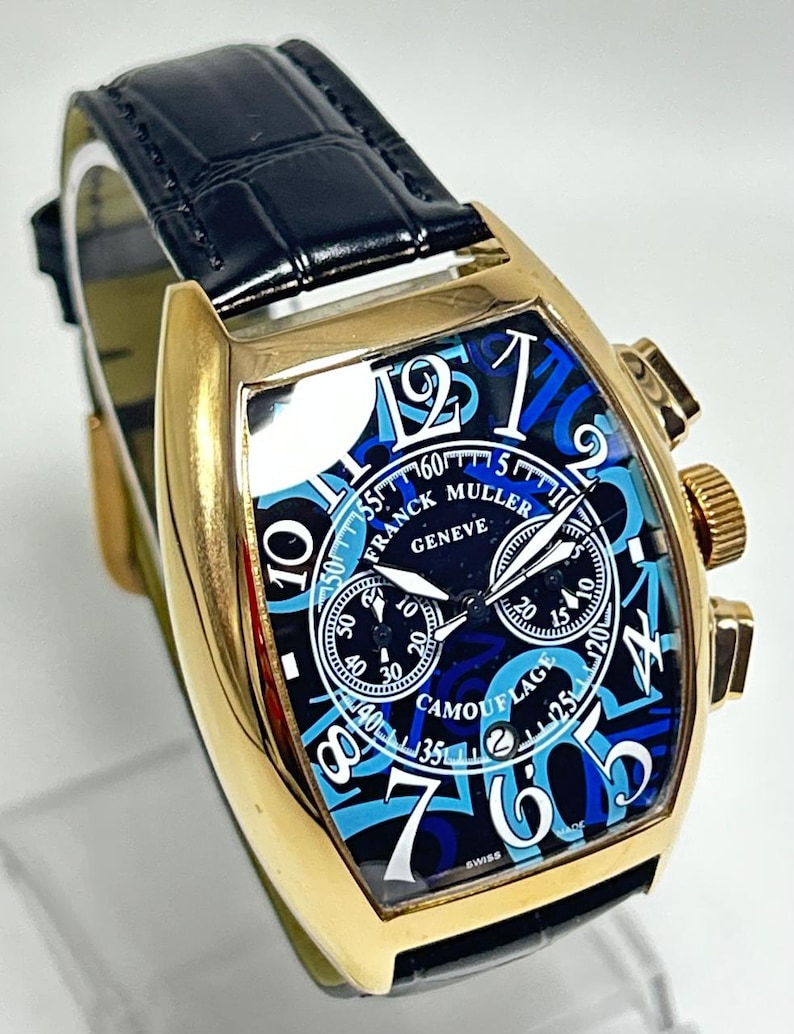 Puede incluir: Un reloj de pulsera dorado con forma de tonel y correa de cuero negro. La esfera presenta un patr&oacute;n de camuflaje azul, grandes n&uacute;meros ar&aacute;bigos blancos y el texto Franck Muller Geneve y Camouflage. Incluye tres subesferas y una ventana de fecha.