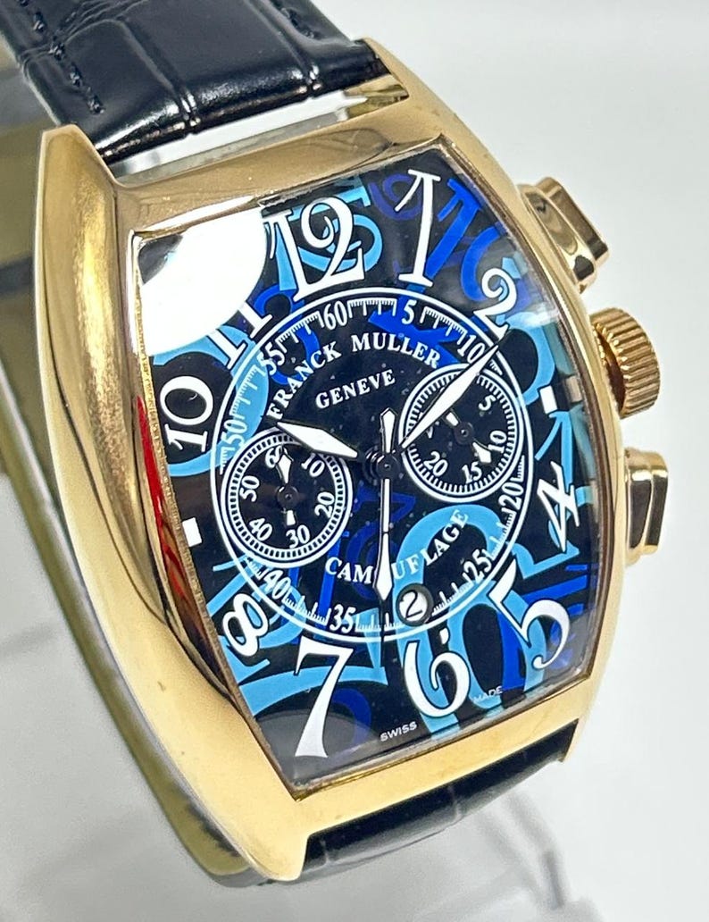 Puede incluir: Un reloj cron&oacute;grafo Franck Muller Geneve en tono dorado con correa de cuero negro. La esfera presenta un patr&oacute;n de camuflaje azul y negro con grandes n&uacute;meros ar&aacute;bigos blancos, tres subesferas, una ventana de fecha y el texto CAMOUFLAGE.