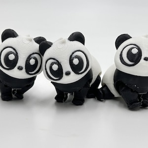 Peut inclure: Trois petites figurines de panda imprim&eacute;es en 3D avec des t&ecirc;tes blanches, de grands contours d'yeux noirs, des oreilles noires et des corps noirs. Chaque panda pr&eacute;sente une t&ecirc;te arrondie et une surface textur&eacute;e, align&eacute;s sur un fond uni.