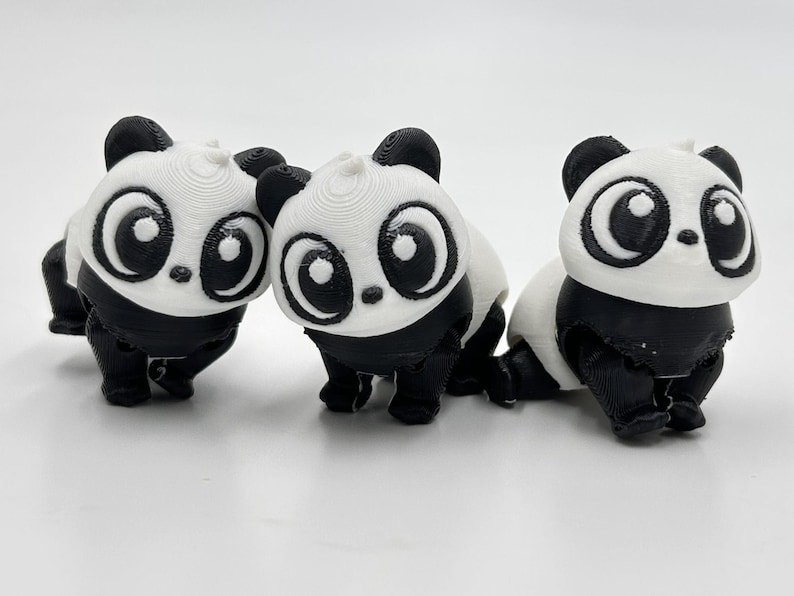 Peut inclure: Trois petites figurines de panda imprim&eacute;es en 3D avec des t&ecirc;tes blanches, de grands contours d'yeux noirs, des oreilles noires et des corps noirs. Chaque panda pr&eacute;sente une t&ecirc;te arrondie et une surface textur&eacute;e, align&eacute;s sur un fond uni.