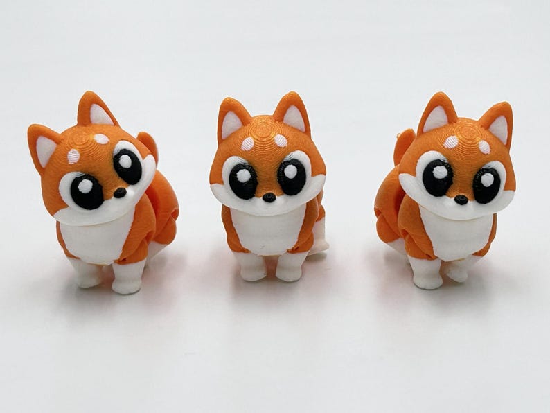 Peut inclure: Trois petites figurines de renards orange et blanc imprim&eacute;es en 3D avec de grands yeux noirs, des marques faciales blanches et des oreilles pointues. Chaque renard est repr&eacute;sent&eacute; debout avec une texture lisse et stratifi&eacute;e sur le plastique.
