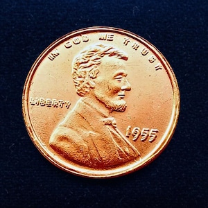 Puede incluir: Una moneda de cobre de Lincoln de 1955. El anverso presenta un perfil de Abraham Lincoln, la palabra "LIBERTY" y la inscripción "IN GOD WE TRUST". El año "1955" es visible debajo de la imagen de Lincoln.