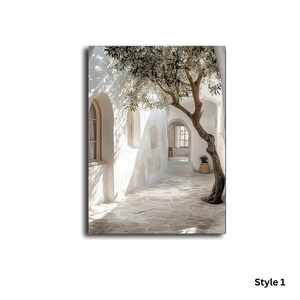 May include: A vertical wall art print depicting a sunlit Mediterranean courtyard with white stucco walls, arched doorways, and a stone-paved ground. A gnarled olive tree with green leaves extends across the scene, casting shadows on the bright walls.