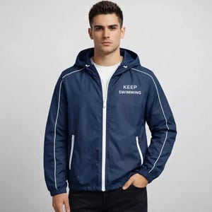 May include: Navy blue hooded jacket with white trim and a white zipper. The jacket has the words "KEEP SWIMMING" printed on the chest. The jacket has two white zippered pockets and a white drawstring hood.
