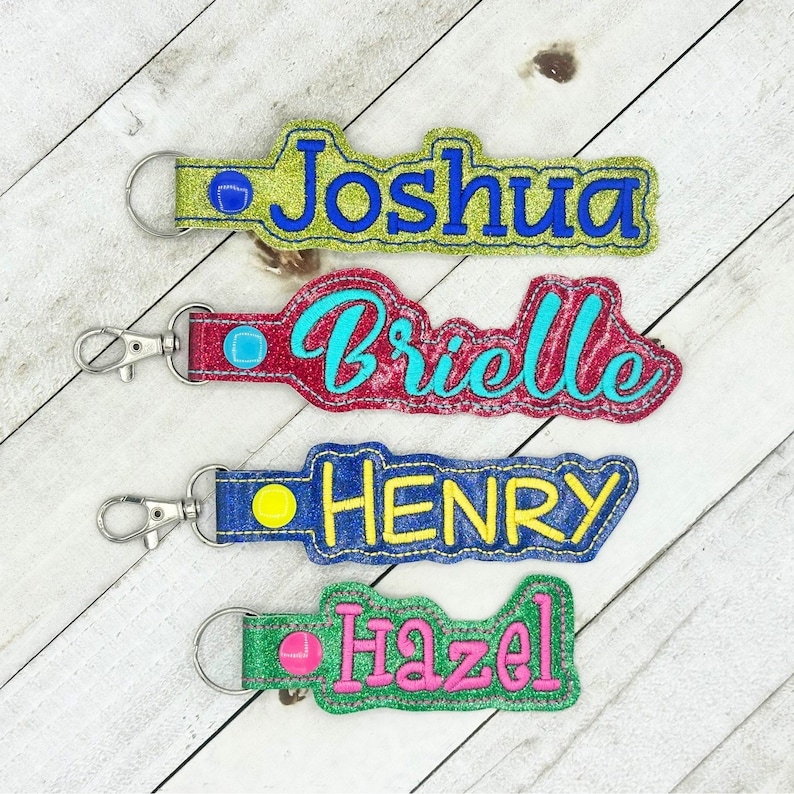 Puede incluir: Cuatro llaveros personalizados con diferentes nombres: Joshua, Brielle, Henry y Hazel. Cada llavero presenta una tela colorida y brillante con un nombre de color contrastante en una fuente decorativa. Los llaveros tienen un anillo de metal plateado y un peque&ntilde;o c&iacute;rculo de colores.