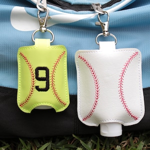 May include: Two baseball-themed hand sanitizer holders with keychains. One is green with the number 9 embroidered on it, and the other is white.