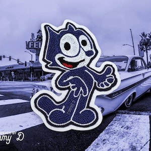 May include: Embroidered patch featuring the cartoon character Felix the Cat in navy blue with white accents and a red mouth. The patch is set against a street scene with a classic car and palm trees.