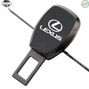 Puede incluir: Un inserto de hebilla de cinturón de seguridad negro con el logotipo y el nombre de la marca Lexus en blanco en la superficie superior. La lengüeta metálica es rectangular con un recorte central, extendiéndose desde una carcasa negra brillante.