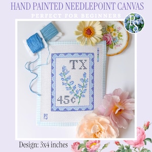 Könnte beinhalten: Eine handbemalte Stickleinwand mit blau-weißem Vichy-Karo-Rand, einem blauen Blumenmuster, dem Text TX und dem Text 45c. Die Leinwand enthält eine blaue Garnrolle und misst 7,62x10,16 cm. Das Design wird zusammen mit Blumen dargestellt.