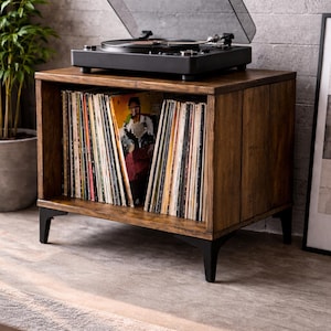 May include: A wooden record player stand with a black turntable on top. The stand has a dark brown finish and black legs. The open shelf is filled with vinyl records. The turntable's dust cover is open.