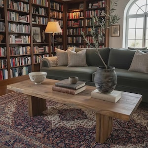 Op de afbeelding: Woonkamer met een houten salontafel, boeken en decoratieve items. Een groene bank met kussens staat achter de tafel. De kamer heeft een vloerkleed met patronen en boekenkasten vol boeken.