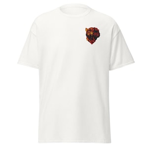 Pode incluir: Uma t-shirt branca de manga curta com um pequeno gráfico detalhado de uma cabeça de tigre a rugir na parte superior esquerda do peito. A ilustração do tigre é apresentada em tons de vermelho escuro, laranja e preto no tecido branco.