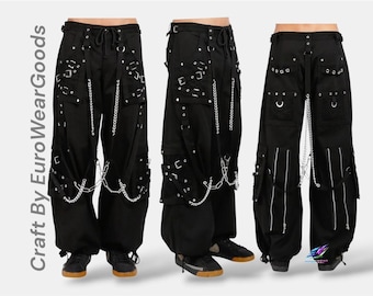 May include: Black cargo pants featuring multiple straps, silver-toned metal buckles, and decorative chains. The pants include side pockets, metal eyelets, and vertical zippers on the lower legs. The text "Craft By EuroWearGoods" is visible.