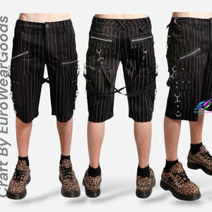May include: Black pinstriped shorts featuring multiple silver-tone zippers, metal D-rings, and adjustable straps. The garment displays the text "Craft By EuroWearGoods" vertically on the left side and a small colorful logo on the right side.