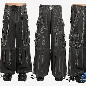 Puede incluir: Pantalones vaqueros negros con múltiples bolsillos, correas y detalles de cadena plateada. Los pantalones tienen cintura con cordón y cremalleras en las piernas. El diseño incluye ojales metálicos y costuras decorativas. Colección Euro Wear.