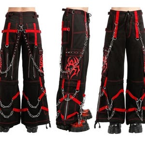 Pode incluir: Calças pretas com detalhes vermelhos, correntes e correias decorativas. As calças têm vários bolsos e um design de perna larga. Costuras vermelhas e um design tribal adicionam detalhes à roupa de inspiração punk.