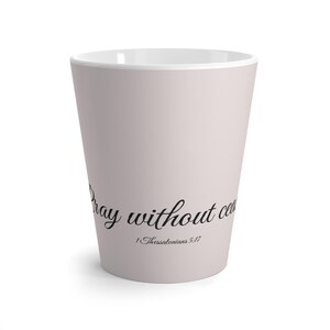 Może przedstawiać: Jasnoróżowy ceramiczny kubek do kawy z napisem "Pray without ceasing" i "1 Thessalonians 5:17" wydrukowanym czarną czcionką. Kubek ma białe wnętrze i zwężający się kształt.