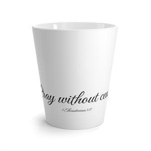 Op de afbeelding: Witte keramische mok met de woorden "Pray without ceasing" in zwart script. De tekst "1 Thessalonians 5:17" staat eronder. De mok heeft een taps toelopend ontwerp.