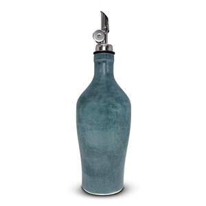 May include: A teal-colored ceramic oil bottle with a stainless steel spout. The bottle has a textured surface and a rounded shape, tapering towards the base. The spout is designed for easy pouring.
